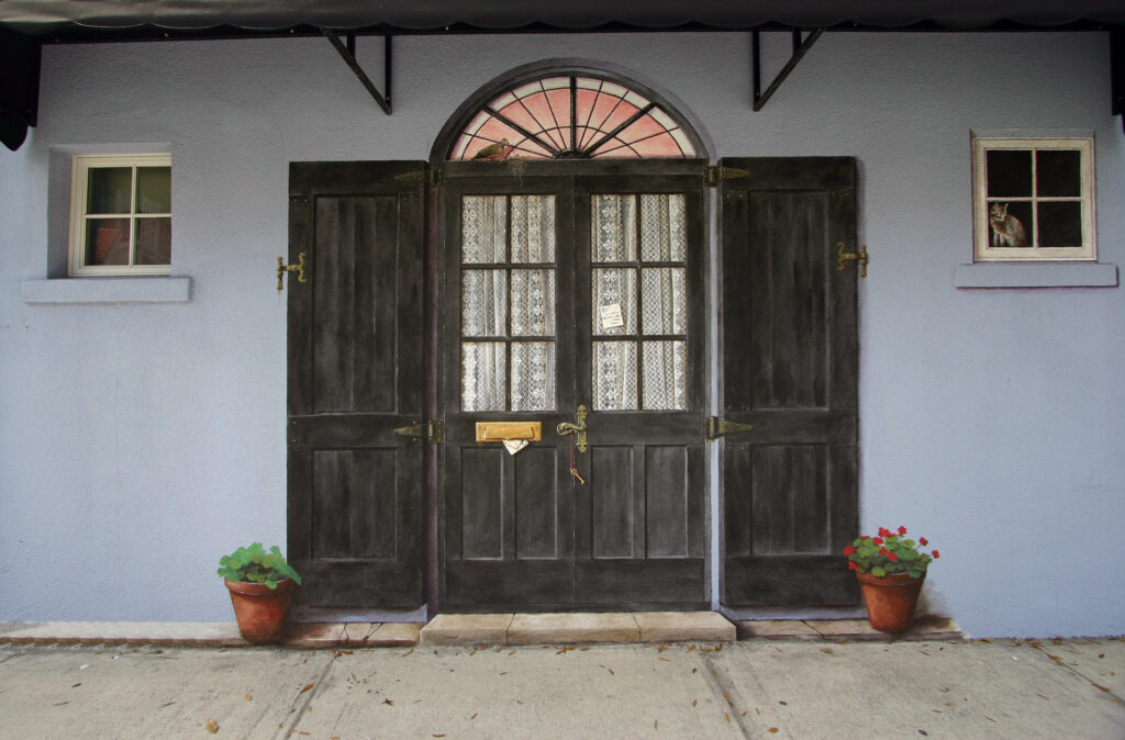 Photo of a mural I painted on an exterior stucco wall in Sarasota, FL. I painted images of two balck doors with lace curtains and black shutters