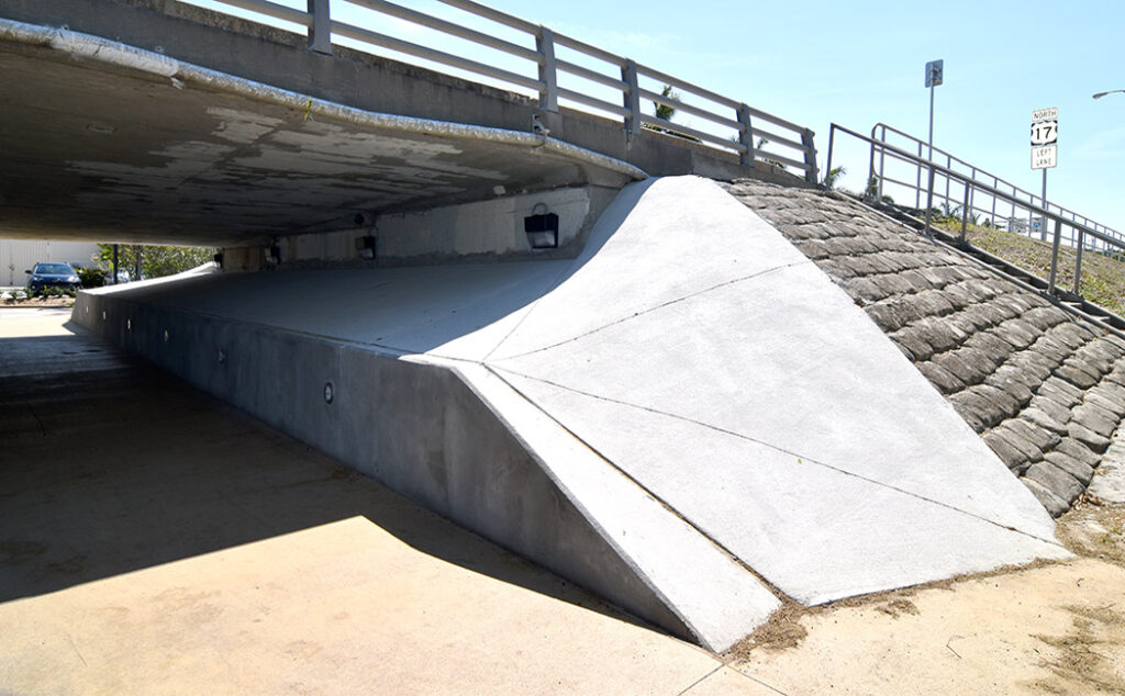 A photo of a potion of a mural I painted under a bridge in Punta Gorda, FL that depicts a series of portholes set into what appears to be old wood. Through each porthole can be seen different species of fish. Before photo
