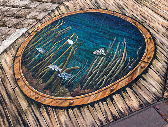 A photo of a potion of a mural I painted under a bridge in Punta Gorda, FL that depicts a series of portholes set into what appears to be old wood. Through each porthole can be seen different species of fish.