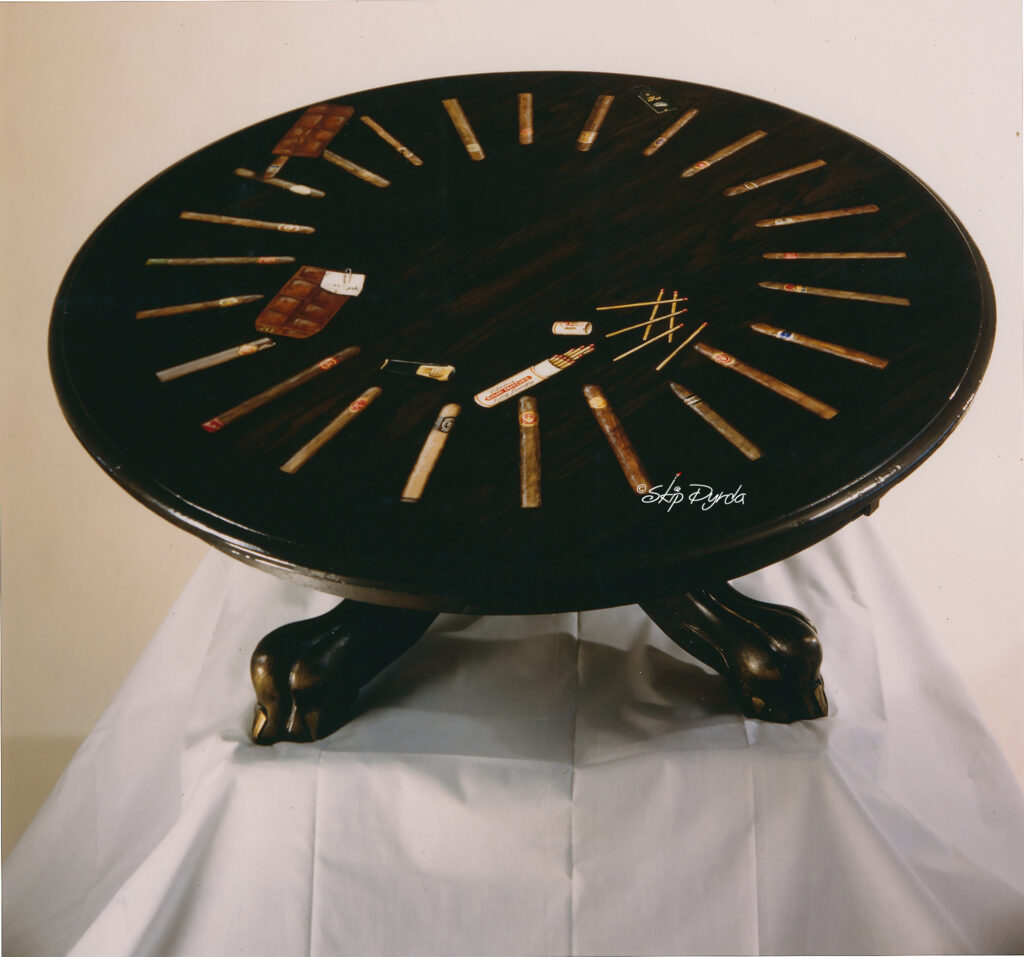 A photo of a large round coffee table that I stained and then painted over 20 Trompe L'oeil cigars on it.